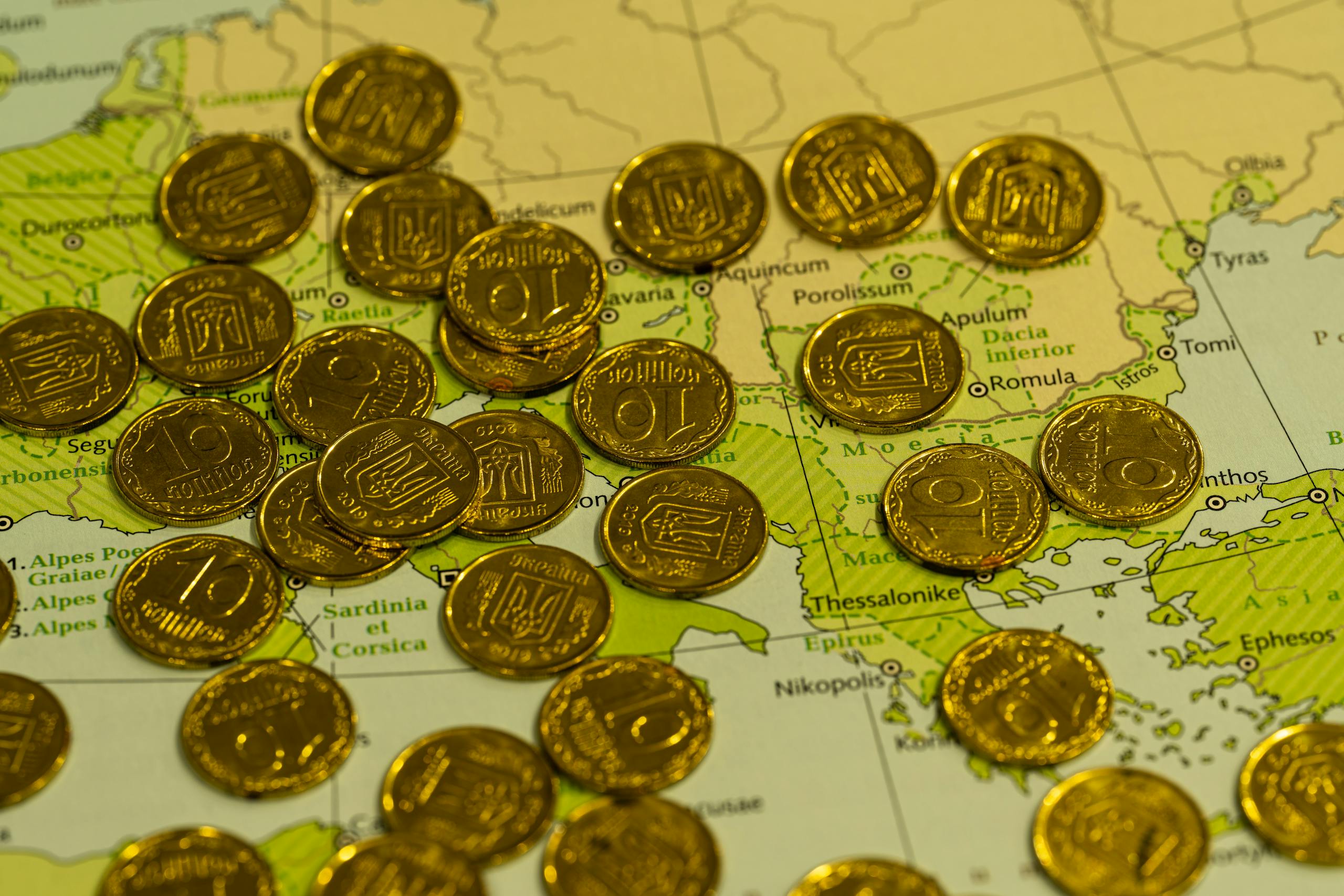 Pile of gold coins placed on top of a detailed geographical map.