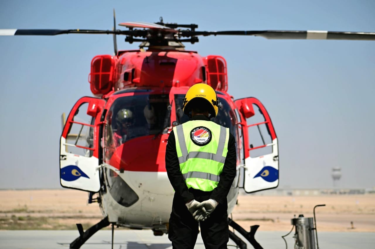 IAF ground crew member standing before a Sarang team ALH Dhruv helicopter before display