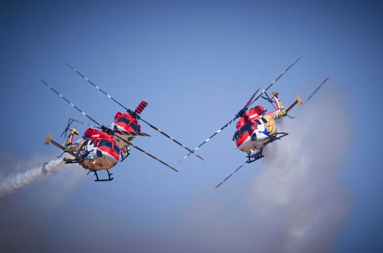 Sarang team helicopters perform a crossing manoeuvre with smoke trails during a formation display